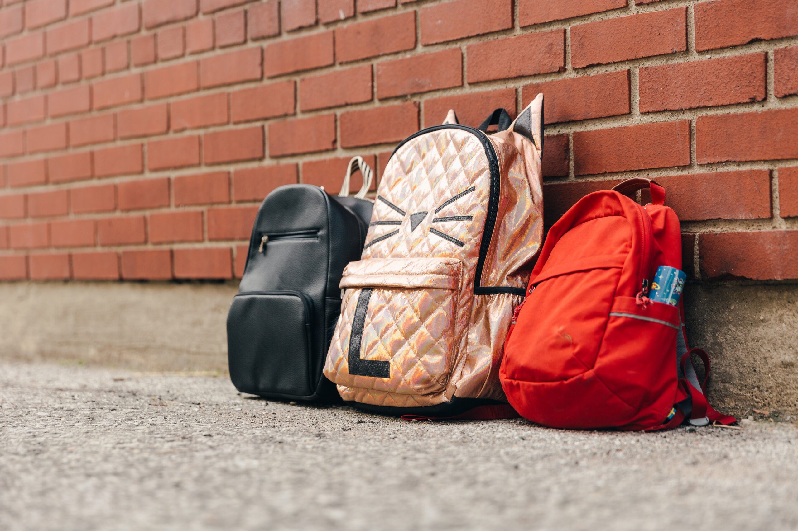 Tres mochilas infantiles y una pared de ladrillo